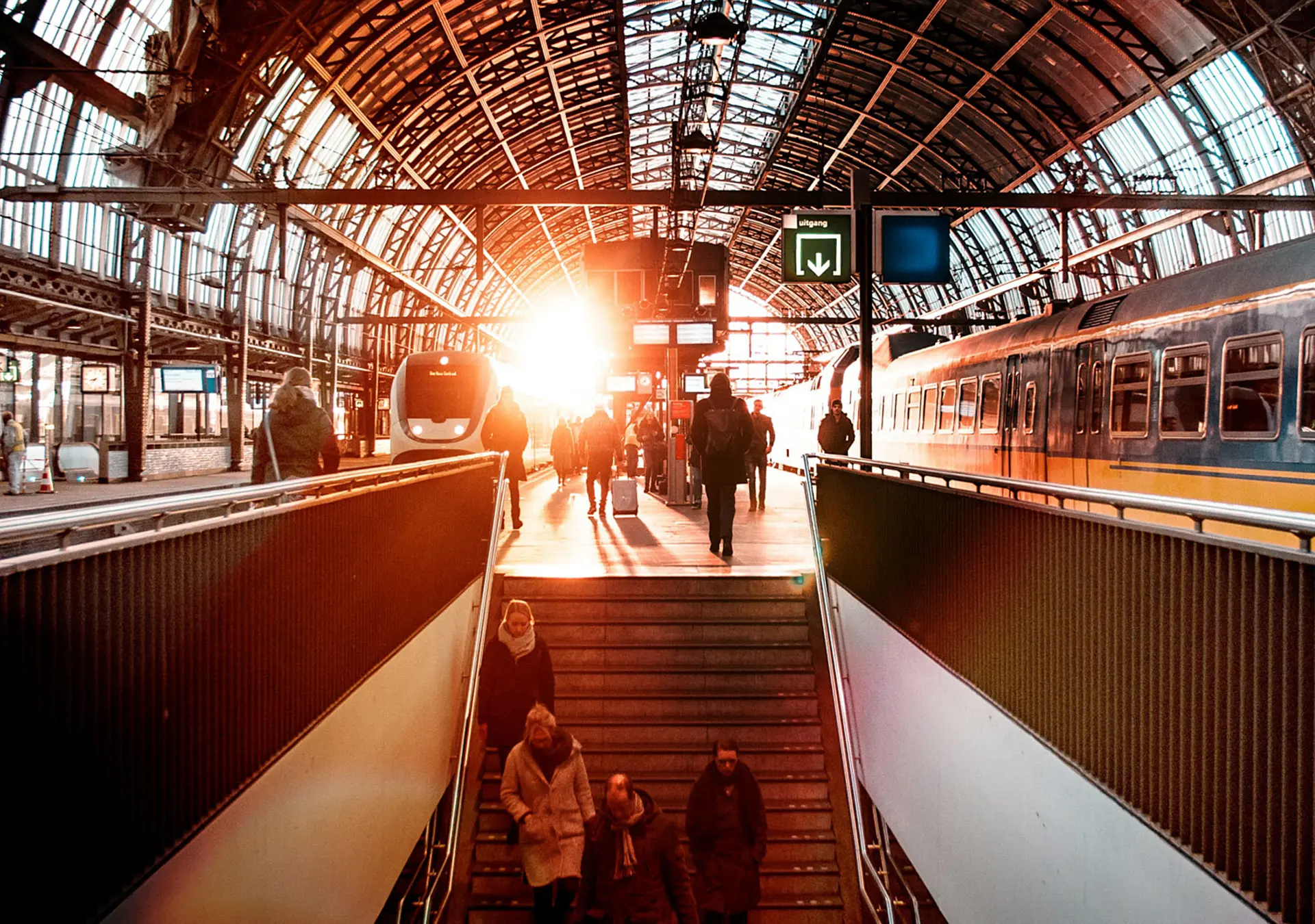 Inside of a train station some people are walking up a flight of stairs to get to the train platform