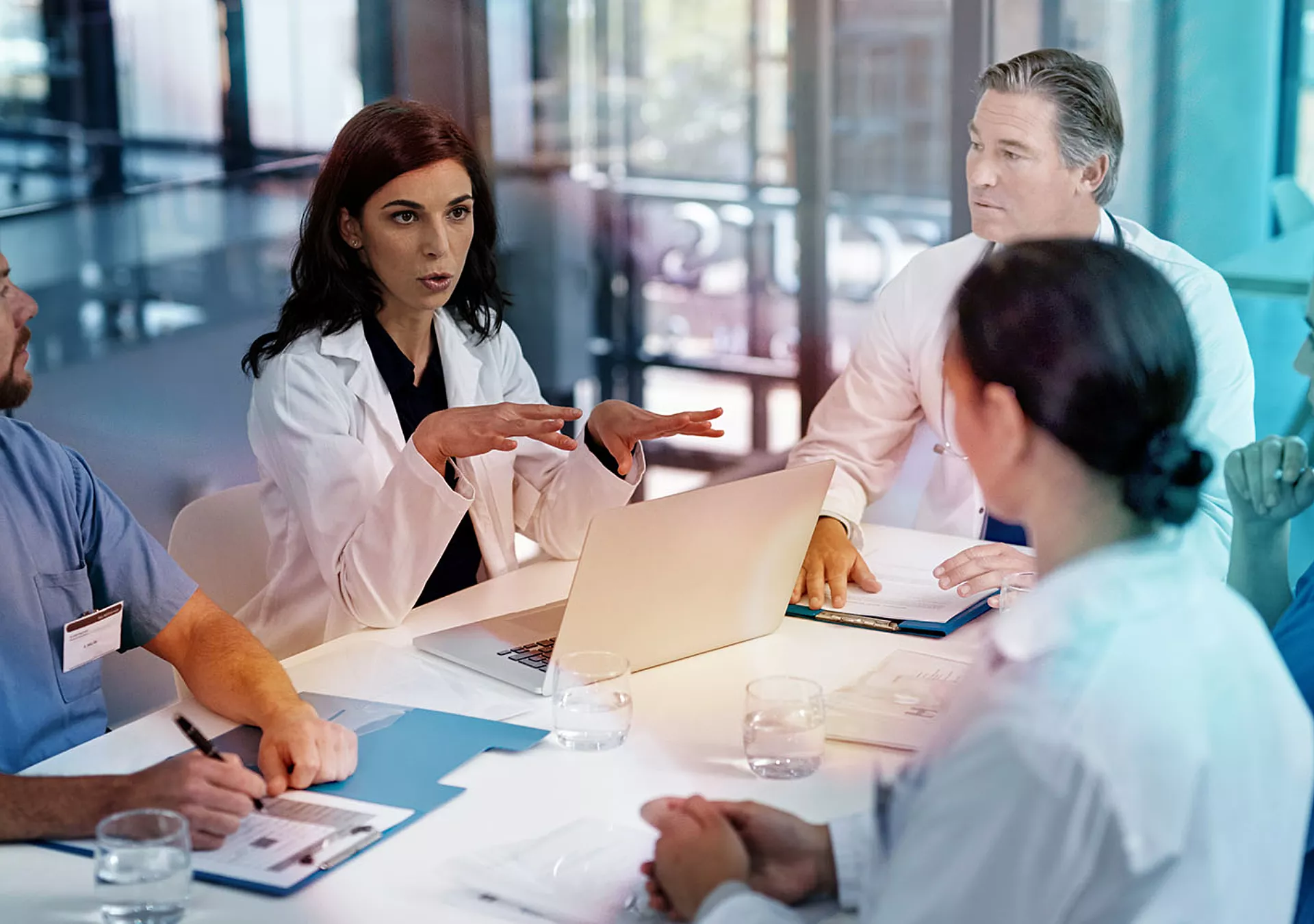 Three doctors and two nurses sitting at a table having a discussion, all have their own notebook
