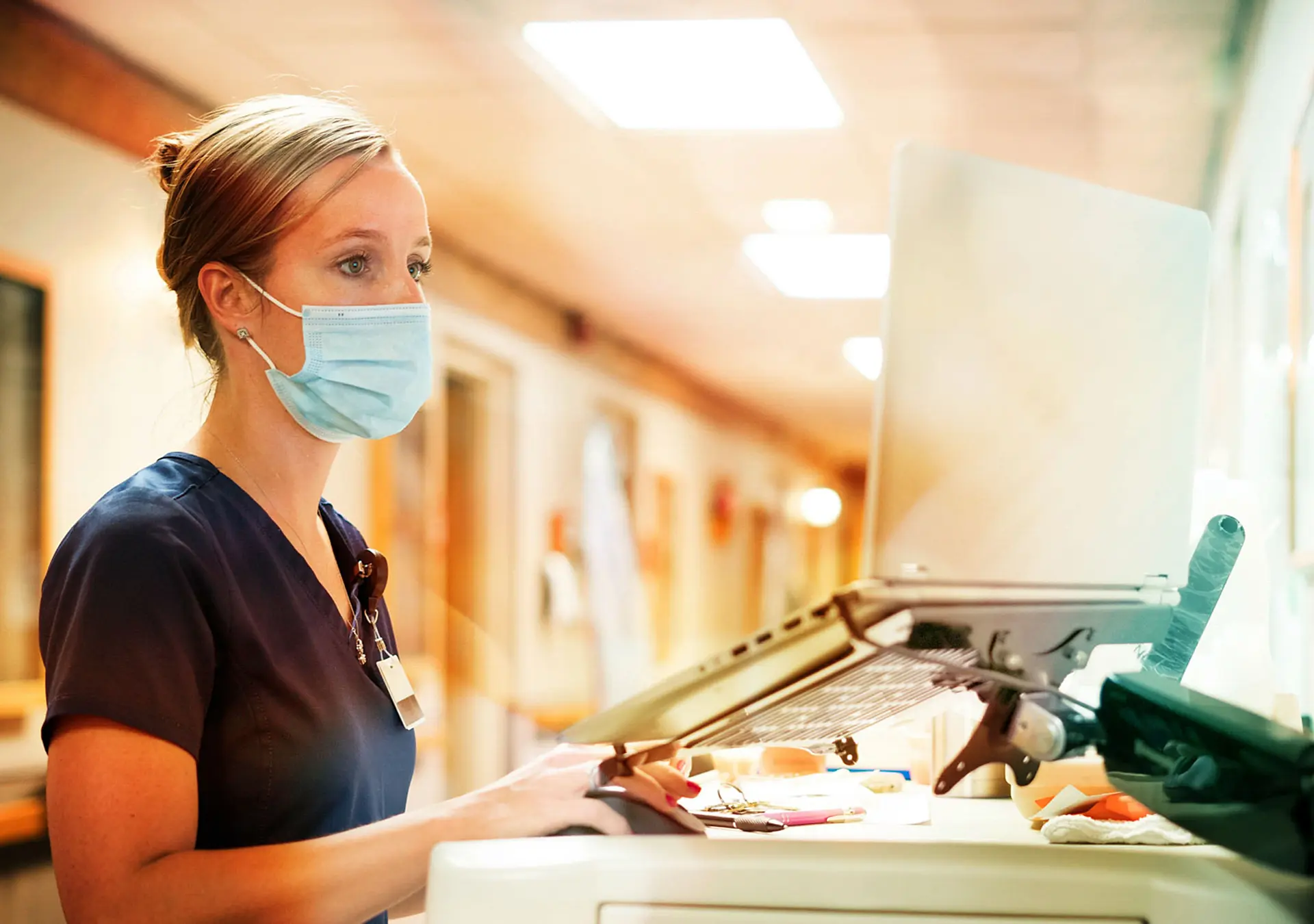 Registered nurse wearing a face mask documents with a laptop computer at the nursing station at work