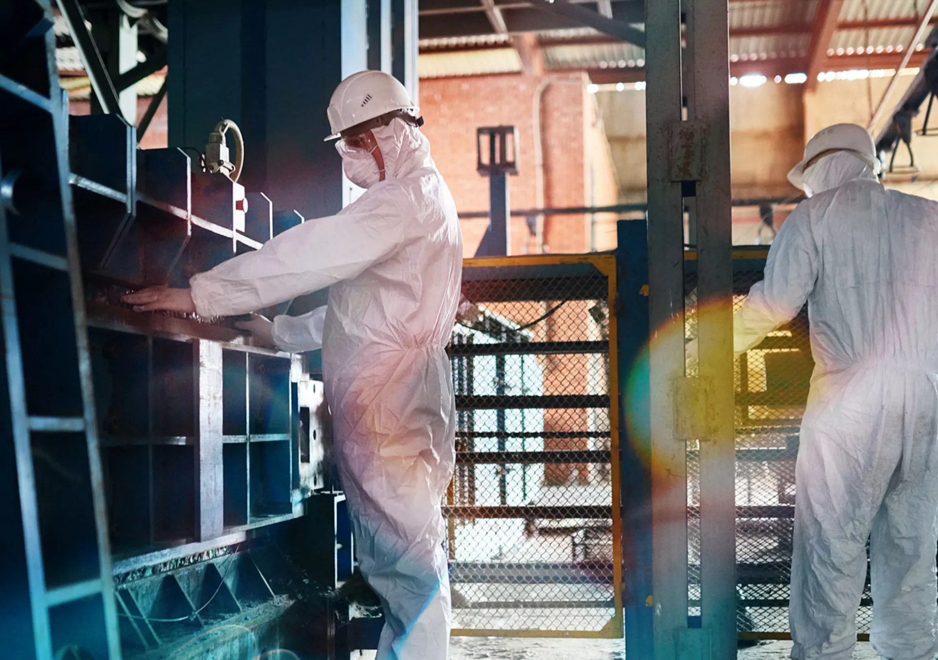 Two workers wearing biohazard suit and hardhats working in open workshop of industrial plant