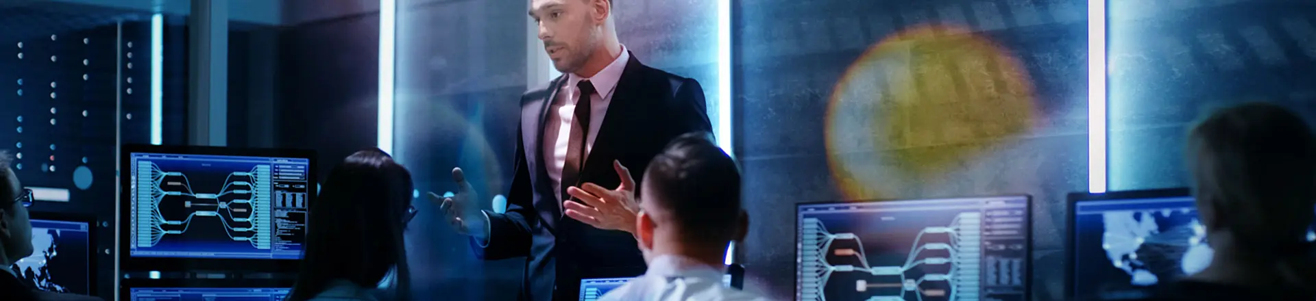 Supervisor Holds Briefing for His Employees in System Control Center Full of Monitors and Servers.