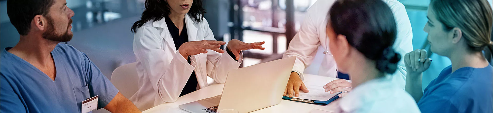 Three doctors and two nurses sitting at a table having a discussion, all have their own notebook
