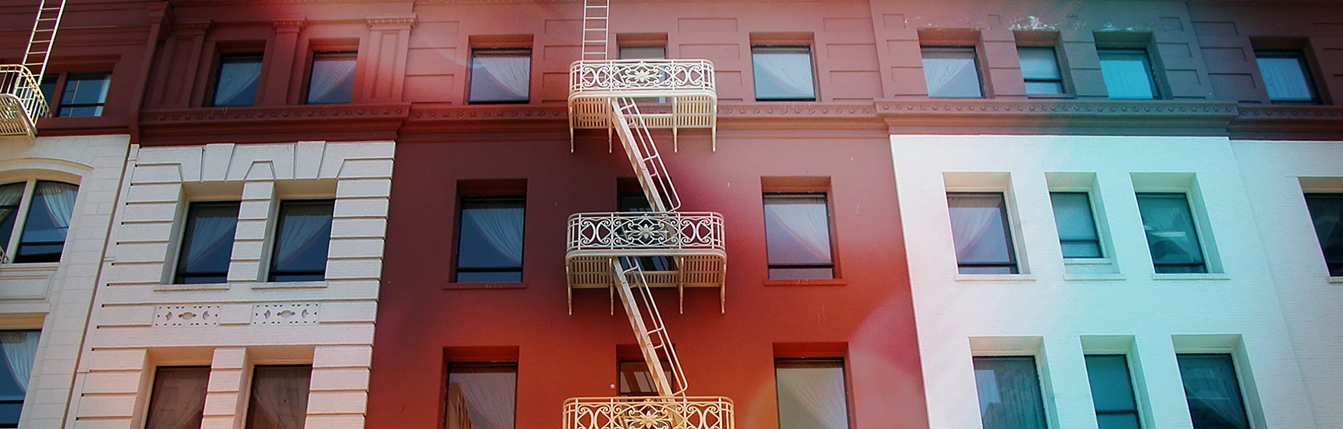 A white fire escape stands out against the red section of a building it snakes up