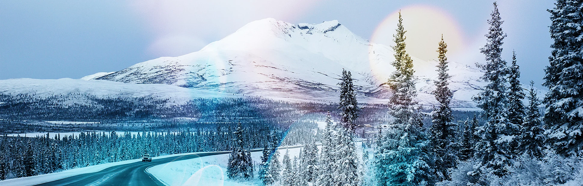 Snow-covered trees surround the highway with a snow-capped mountain in the background