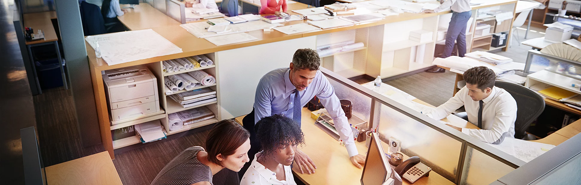 Colleagues working at a woman's workstation in a busy office