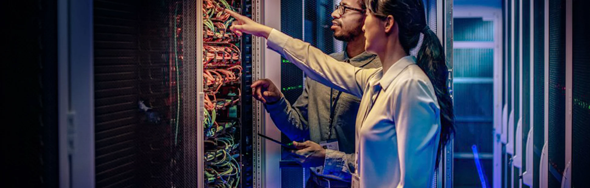 Male and female IT engineers checking servers in server room with help of tablet.