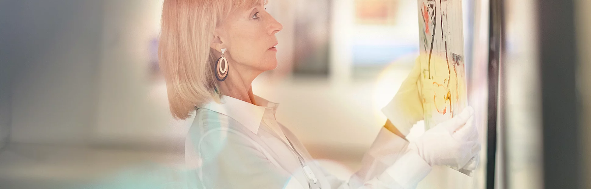 Side view portrait of elegant mature woman hanging paintings while working in modern art gallery