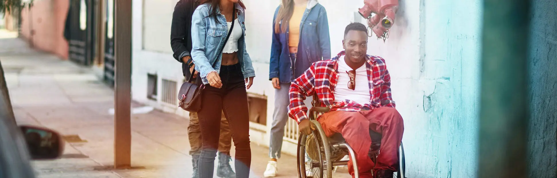 People walking with their male friend in a wheelchair on a city sidewalk wearing casual clothes