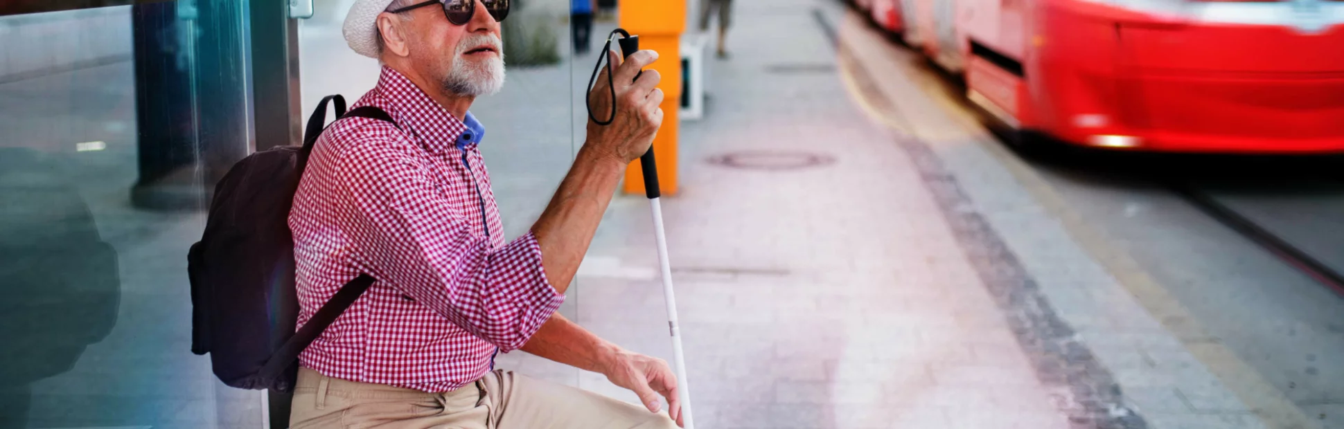 Senior blind man sitting on bench with white cane waiting for public transport in city