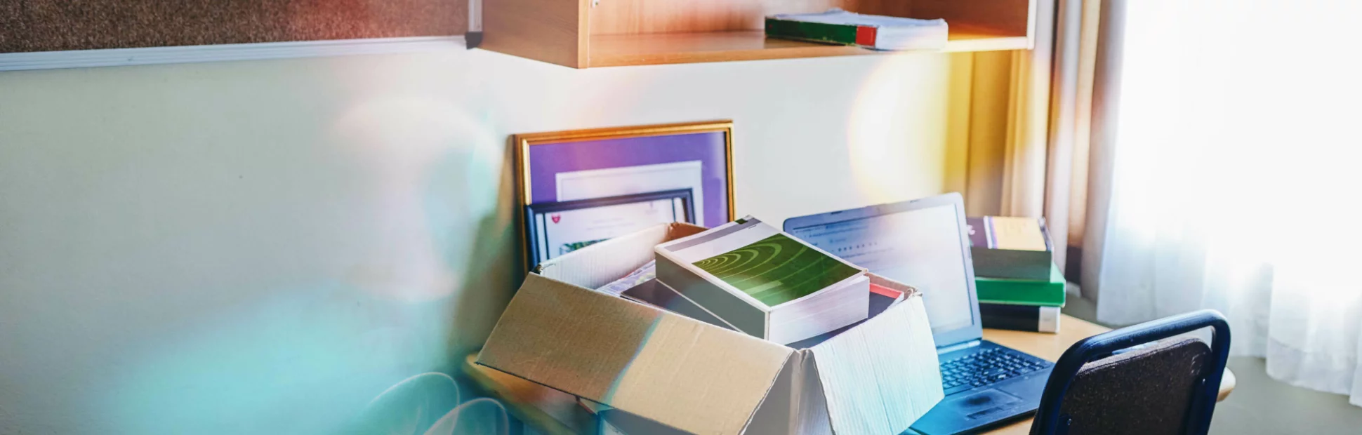 Small desk in a room with a box of books and personal items in it next to a computer