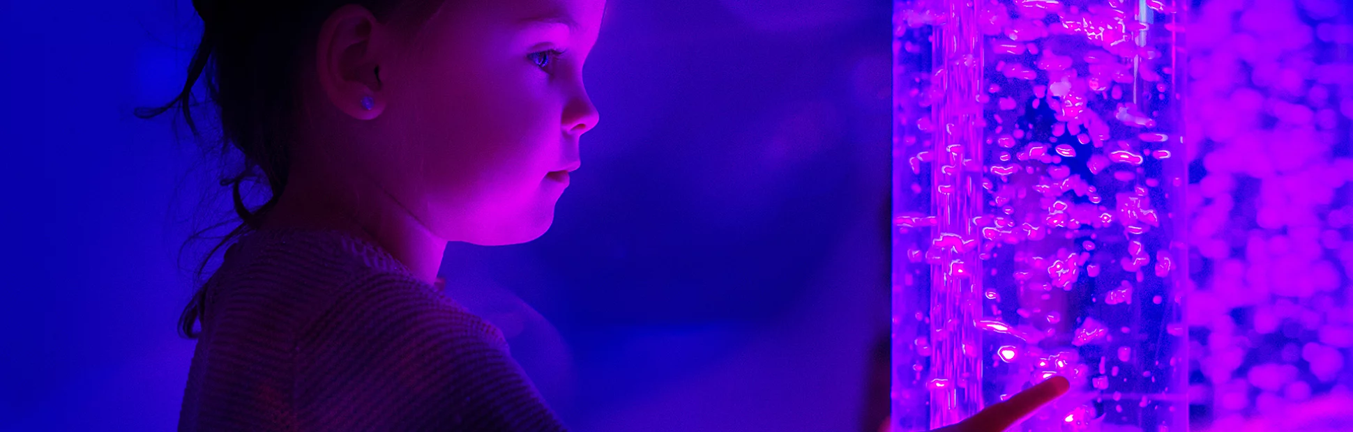 Child in therapy sensory stimulating room interacting with colored lights bubble tube