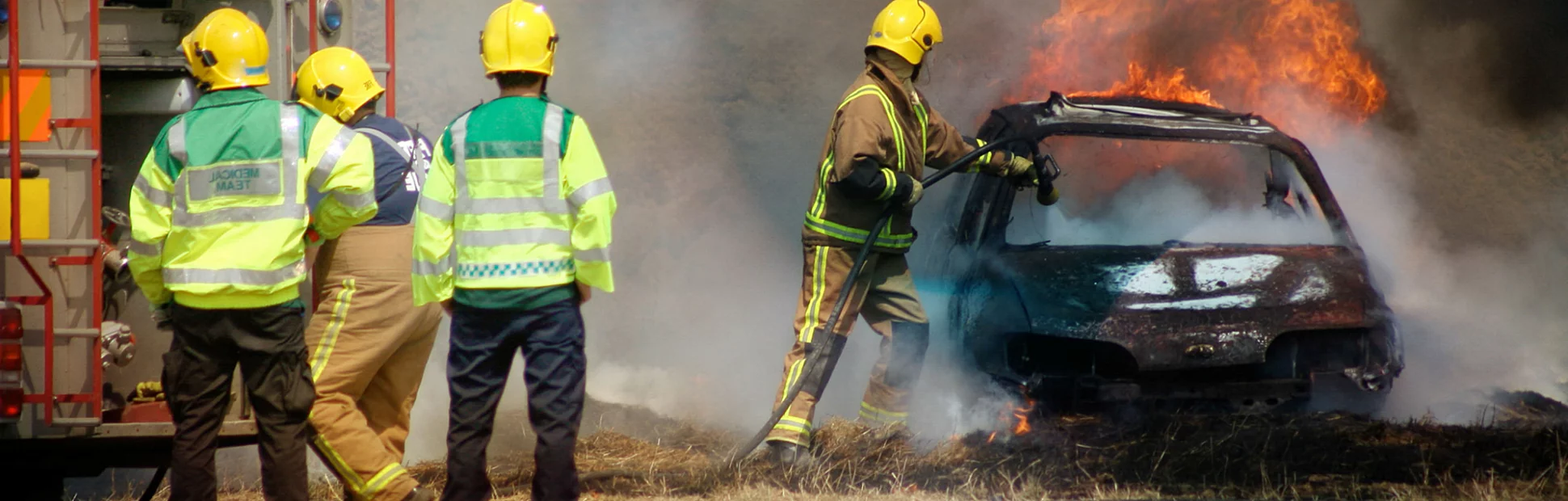 Firefighters in full fire fighting equipment putting out a car fire