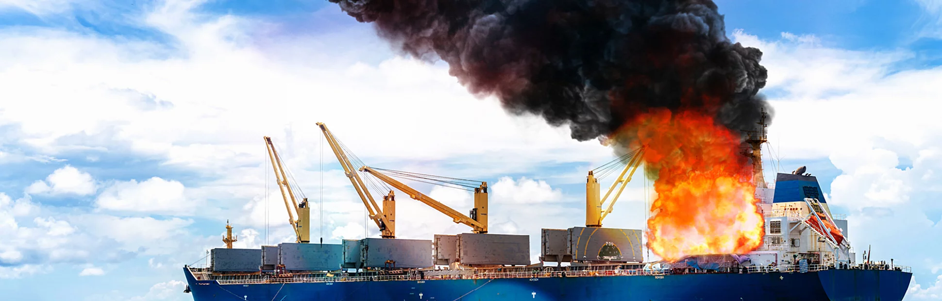 Large general cargo ship on fire and lots of smoke out at sea on a bright day