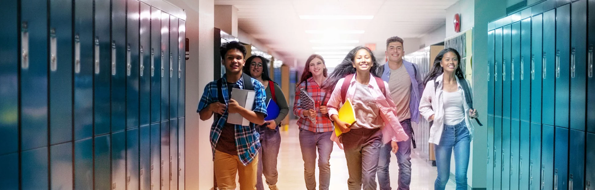 Cheerful male and female students running in illuminated corridor.