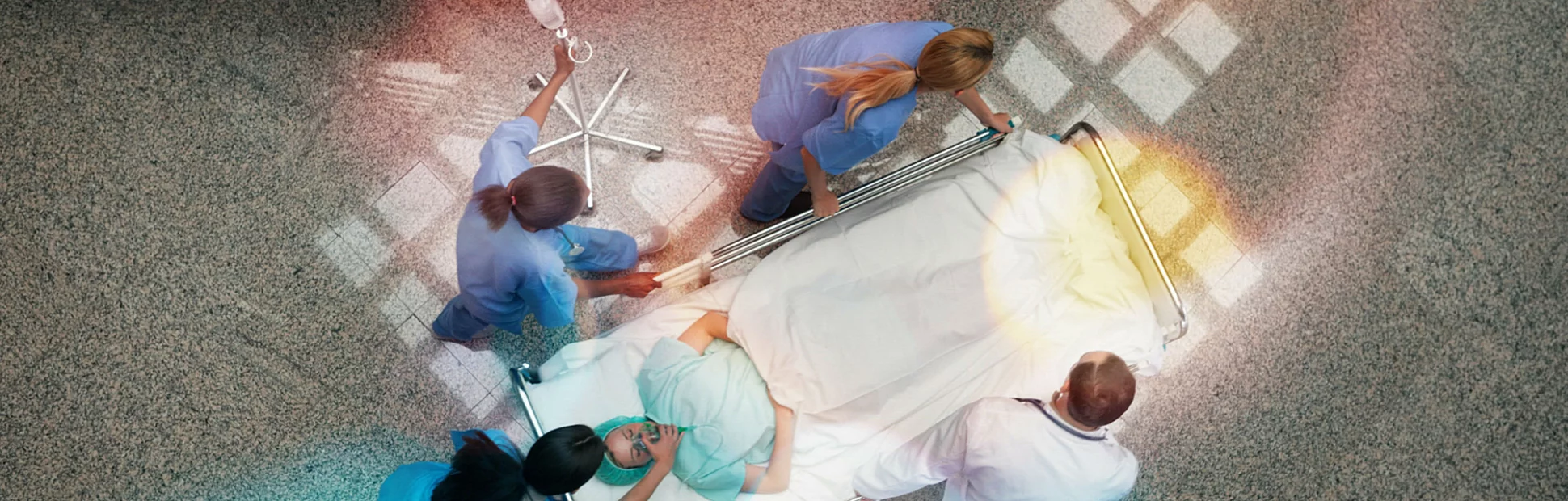 Three nurses and one doctor pushing one patient in a bed in hospital corridor