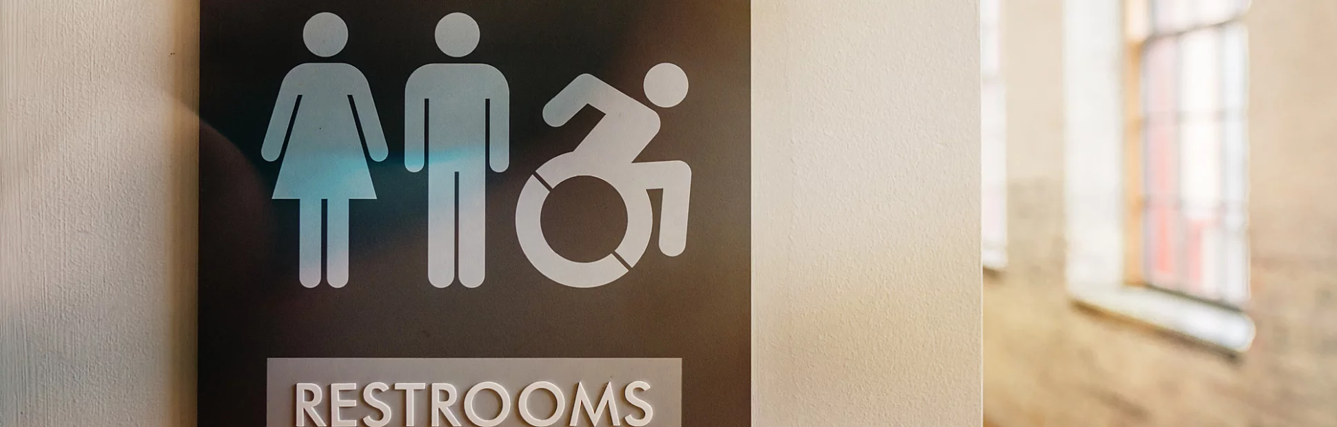 Unisex bathroom sign against neutral colored wall with symbols for male, female, and wheelchair.