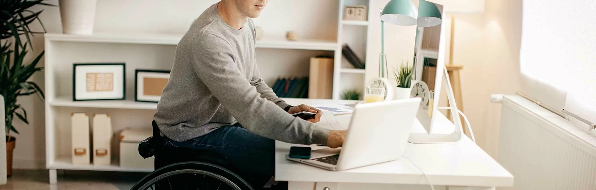 Young man in a wheelchair working on his laptop at his desk