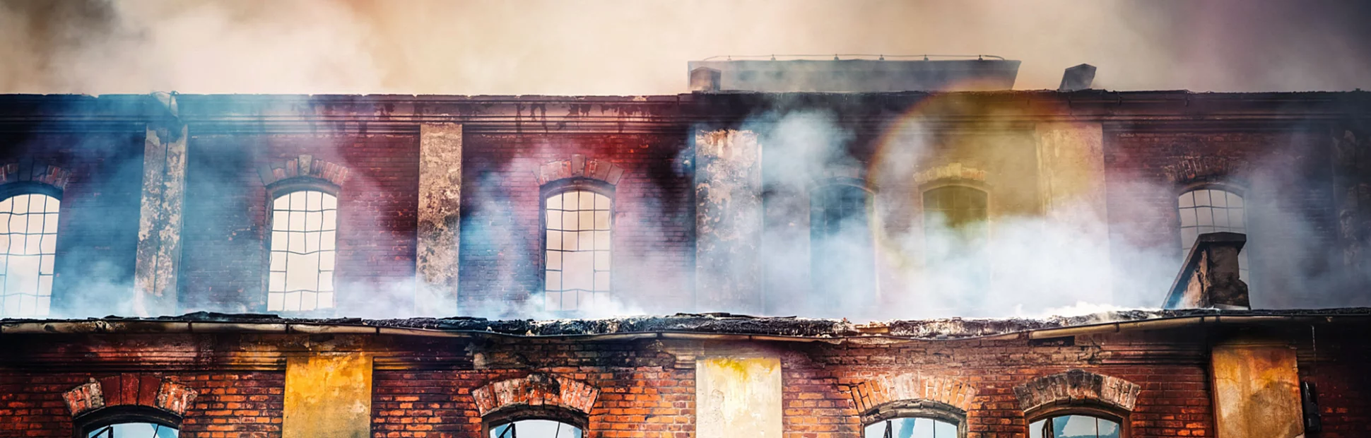 Photo of a burning old red-brick factory with a lot of smoke.