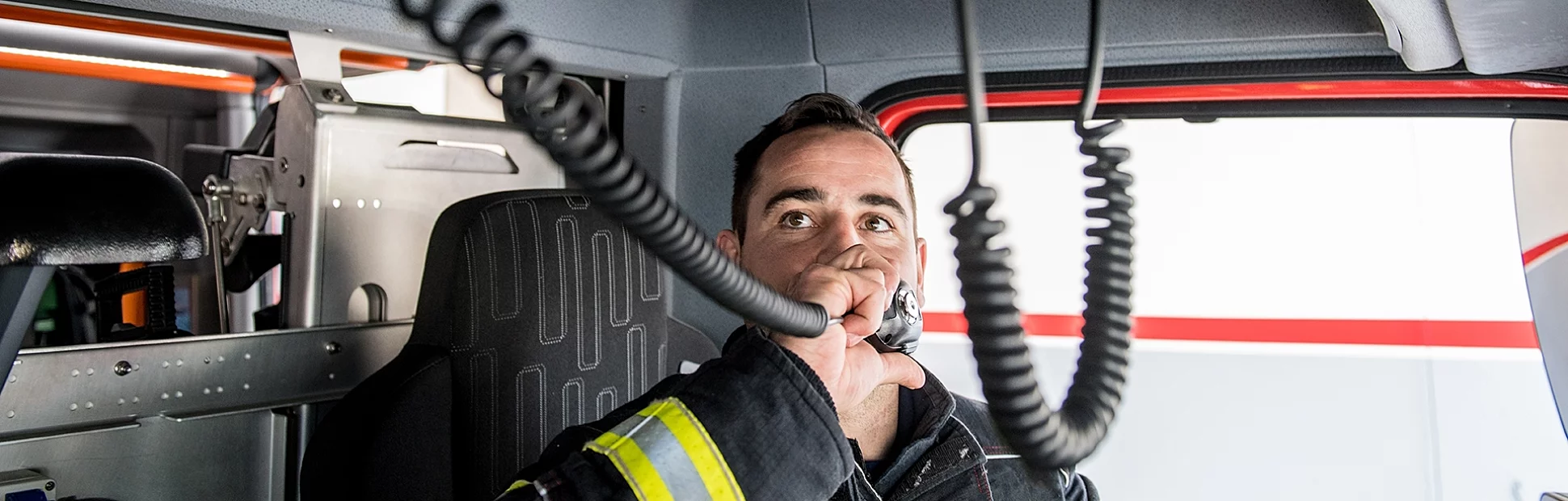 Male firefighter in the driver's seat of a fire truck using the handheld radio