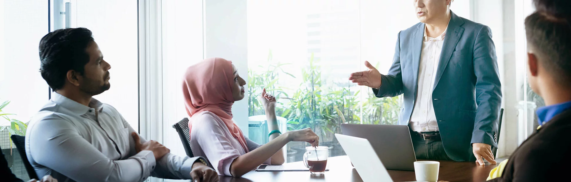Multi racial group of business people sitting around meeting table and listening to male manager