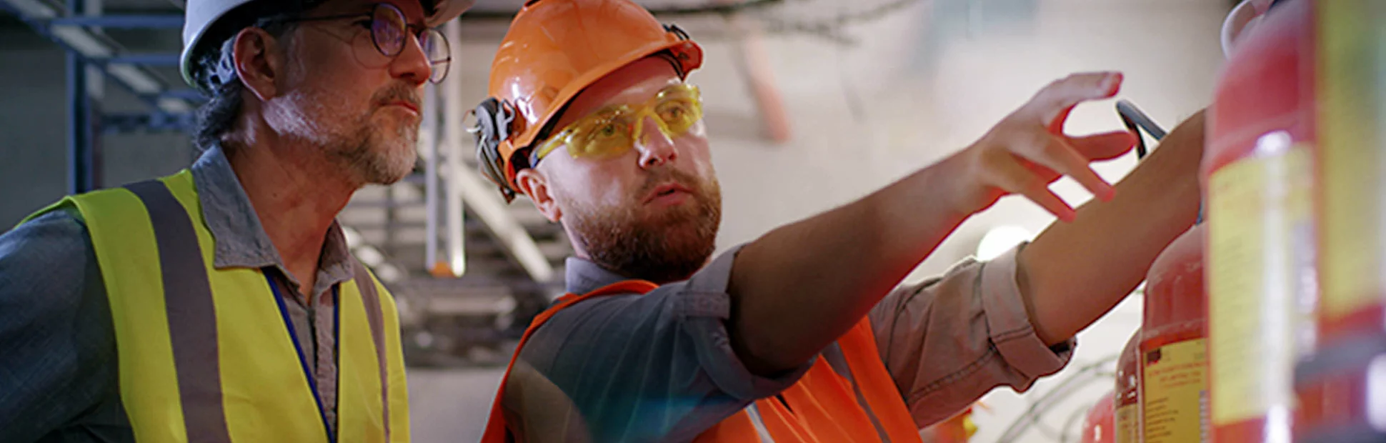 Bearded worker demonstrating fire extinguishers to mature inspector while working on power station