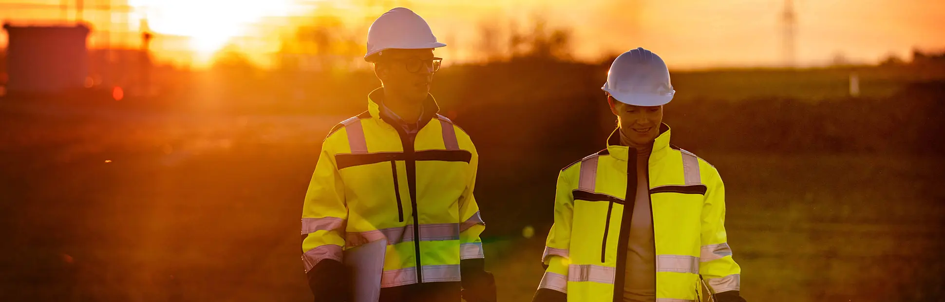 Two engineers discussing while walking on rural field during sunset