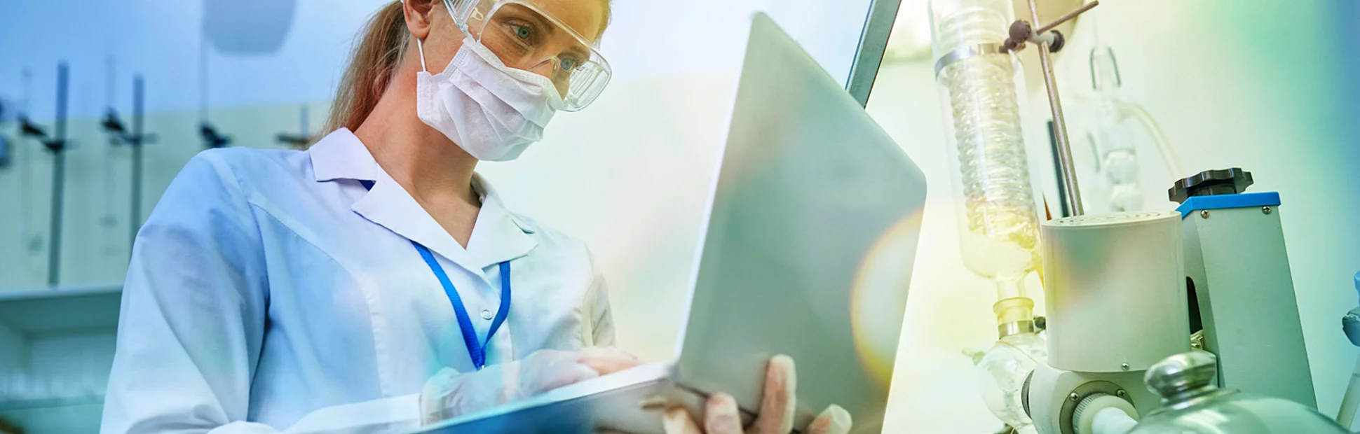 confident young female scientist in protective mask and safety goggles using laptop