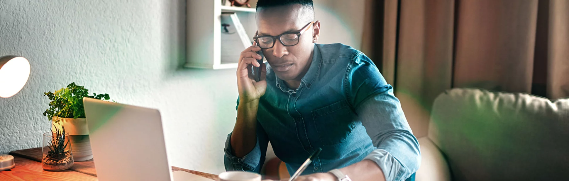 young businessman sitting alone in his office and talking on his cellphone while making notes