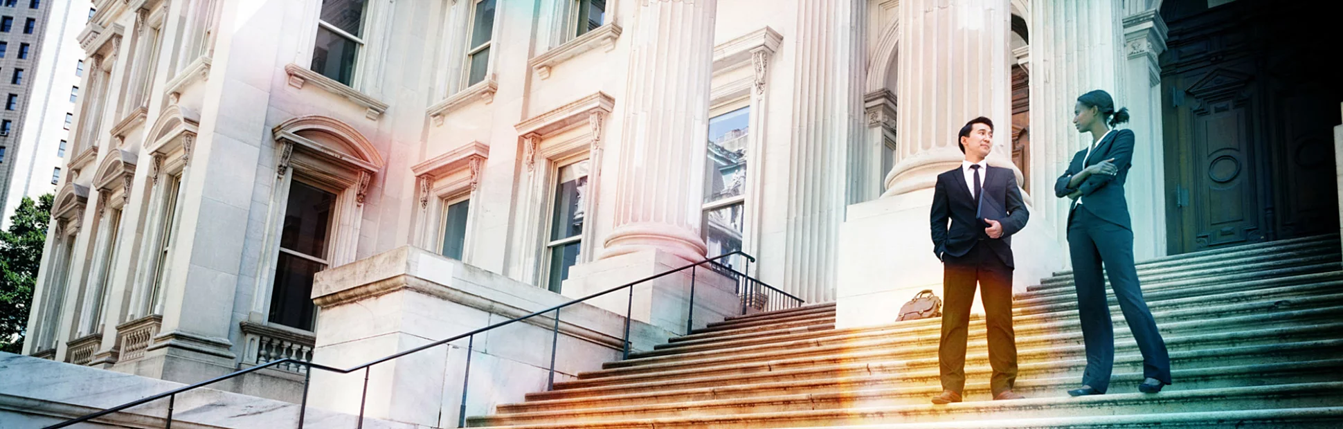 A well dressed man and woman converse on the steps of a legal or municipal building.