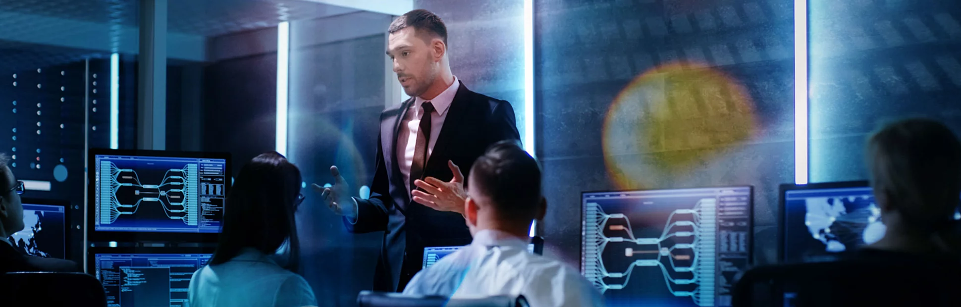 Supervisor Holds Briefing for His Employees in System Control Center Full of Monitors and Servers.