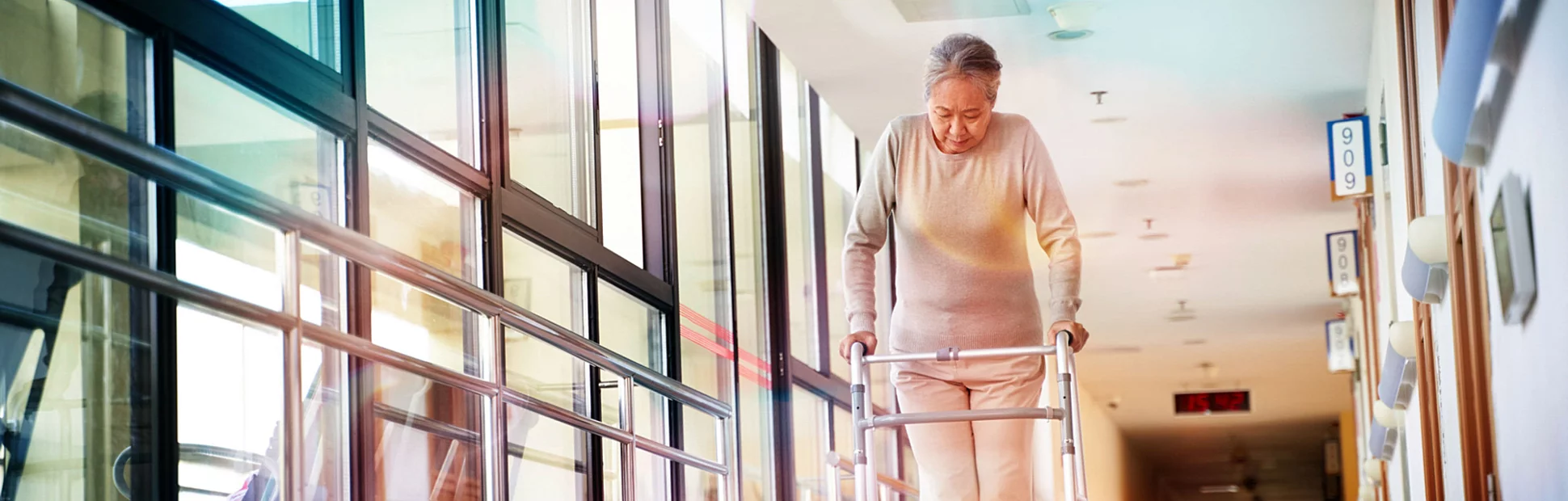 elderly woman walking using a walker in hall way of nursing home, low angle view.