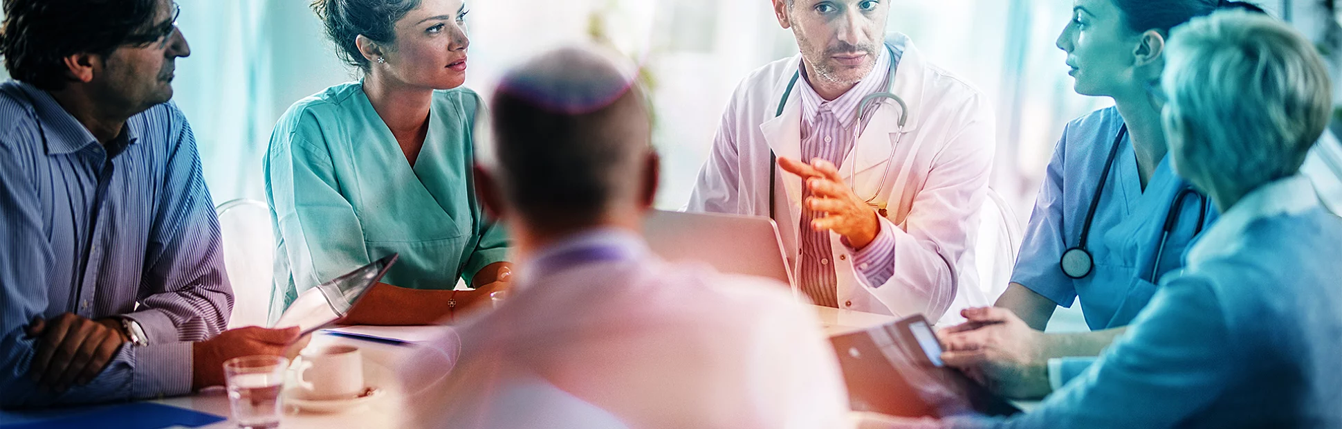 Male doctor and his female colleagues talking to team of business people at a meeting