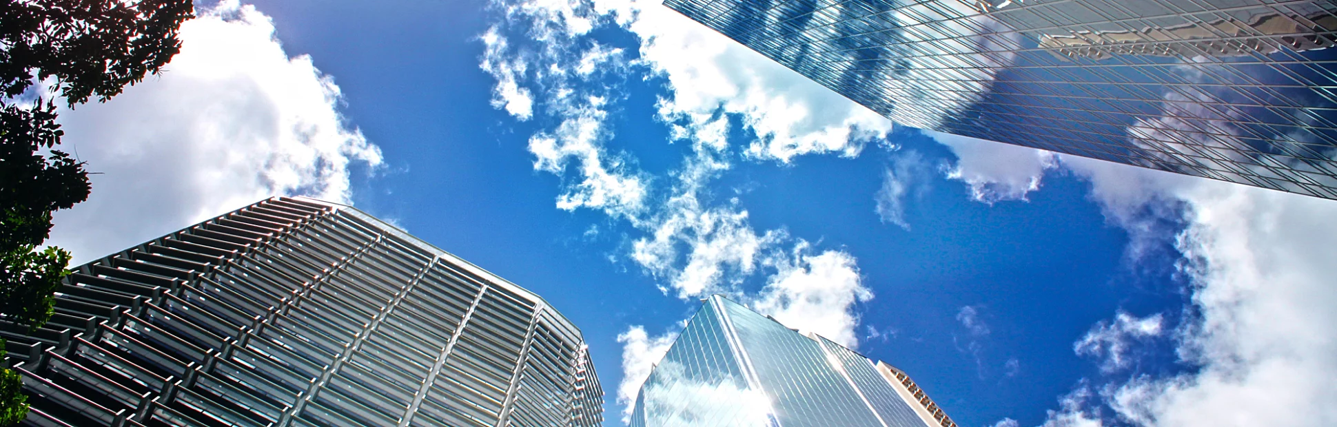 View looking up at blue cloudy sky through skyscrapers reflecting clouds and other buildings