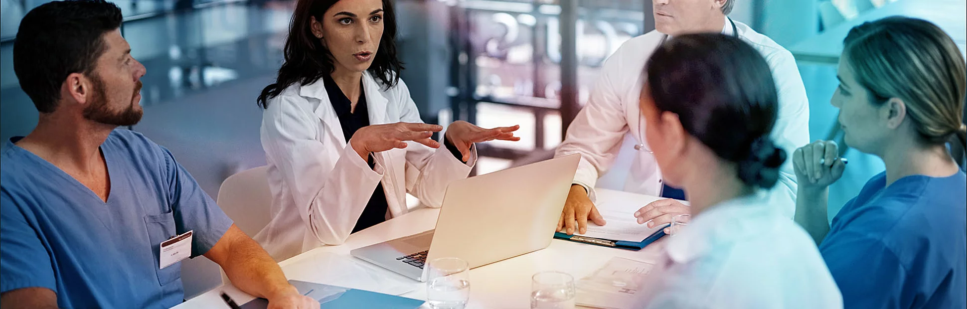 Three doctors and two nurses sitting at a table having a discussion, all have their own notebook