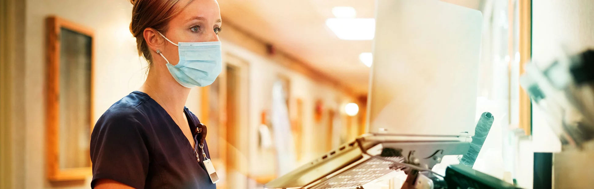 Registered nurse wearing a face mask documents with a laptop computer at the nursing station at work