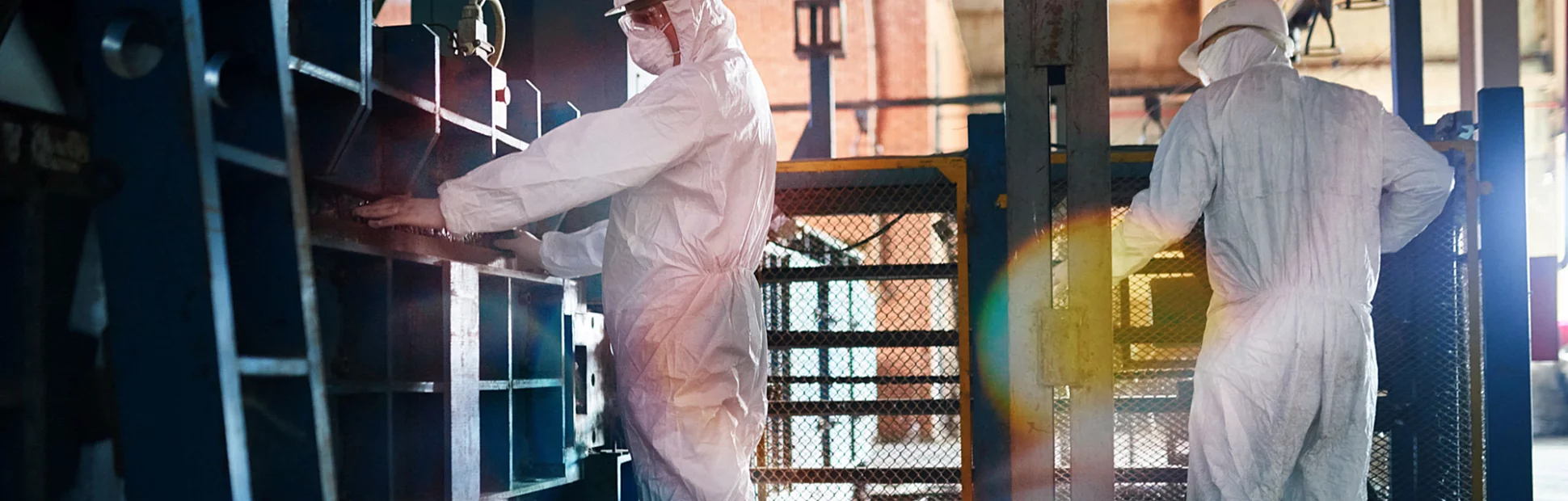 Two workers wearing biohazard suit and hardhats working in open workshop of industrial plant
