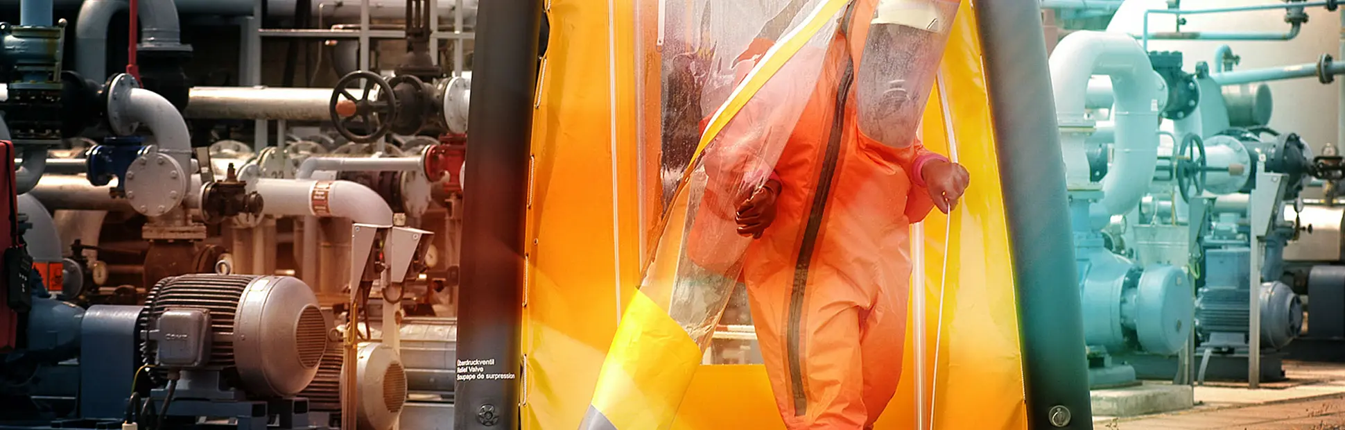 A worker in an orange hazmat suit exits an inflatable decontamination tent at an industrial facility