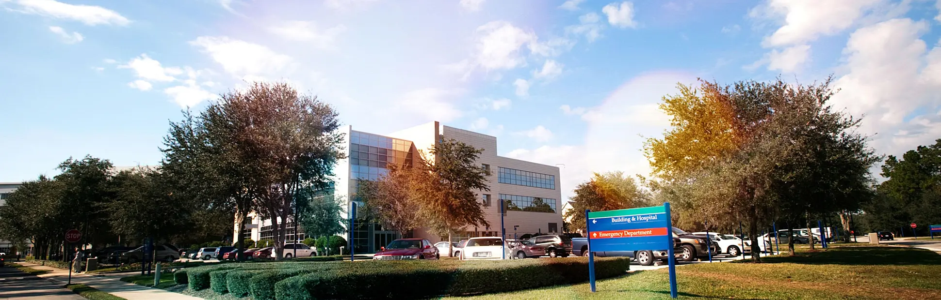 Modern building and parking lot under a partly cloudy sky. Lush trees surround the area.