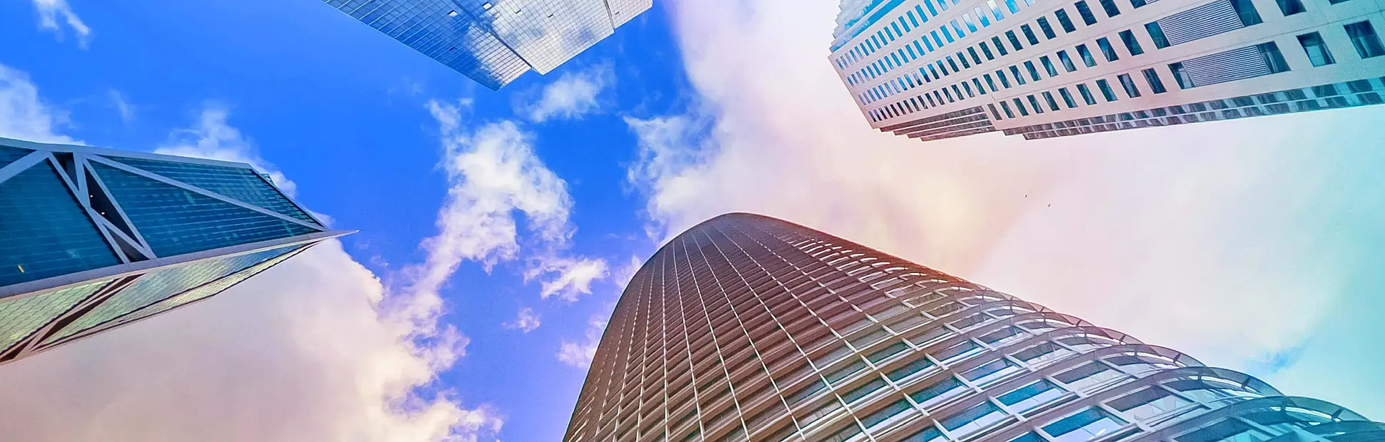 Skyward view of modern, glass & steel skyscrapers against a vivid blue sky with scattered clouds.