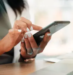 woman at desk with laptop, holding and using her smartphone