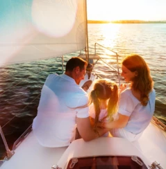 Parents And Little Daughter Sitting Together On Sailboat Deck Hugging Enjoying Sea Trip.