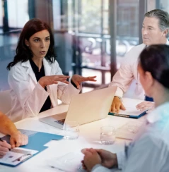 Three doctors and two nurses sitting at a table having a discussion, all have their own notebook