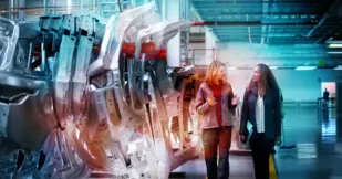 Female engineers discussing by car chassis walking on an aisle in a factory. 