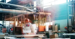 Determined craftsman is working in carpentry workshop. He is examining paper.