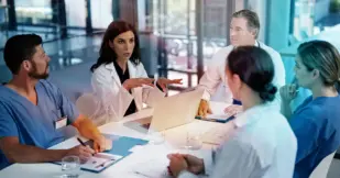 Three doctors and two nurses sitting at a table having a discussion, all have their own notebook