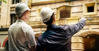 Two engineers in white hard hats pointing at a building