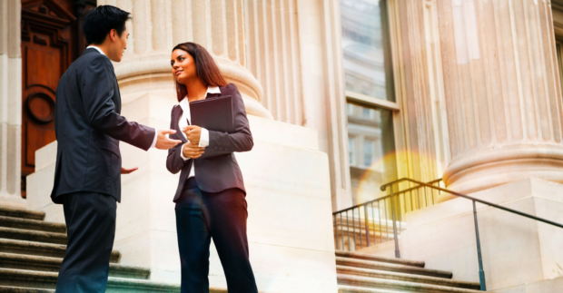 Professional woman and man having a discussion on the stairs of a stately building.