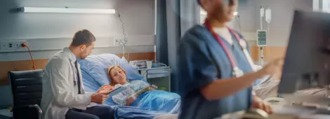 Female Head Nurse Uses Medical Computer, In the Background a Doctor is Consulting a Patient