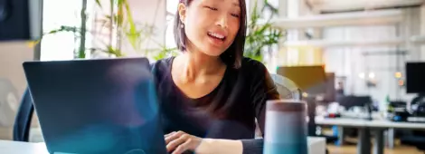  Female professional working on laptop and talking into a speaker.