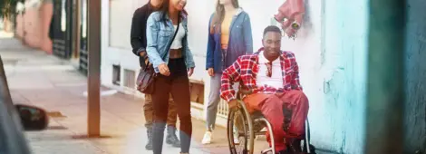 People walking with their male friend in a wheelchair on a city sidewalk wearing casual clothes